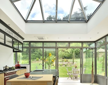 Espace cuisine lumineux avec véranda moderne signée Vérand'Art Pour sublimer le cachet de cette cuisine industrielle authentique, une grande véranda est installée face au jardin pour ensoleiller la pièce et lui donner une déco moderne.