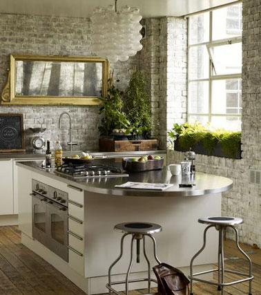 Beau mélange industriel et déco recup dans la cuisine américaine avec mur en brique blanc et parquet brut. Modernisés avec des meubles de cuisine laqué blanc et de l'électroménager inox