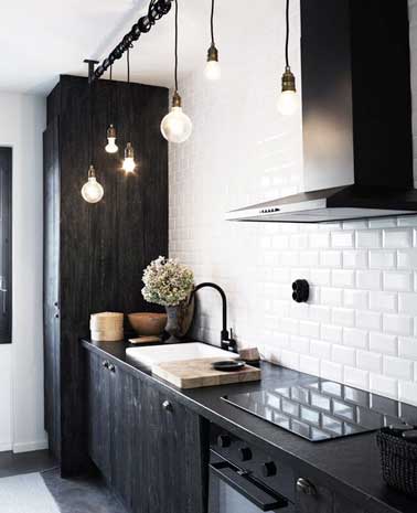 Cuisine design noir et blanche avec carrelage métro et meubles de cuisine noirs. Valorisé par un linéaire suspension style loft et une hotte en inox.