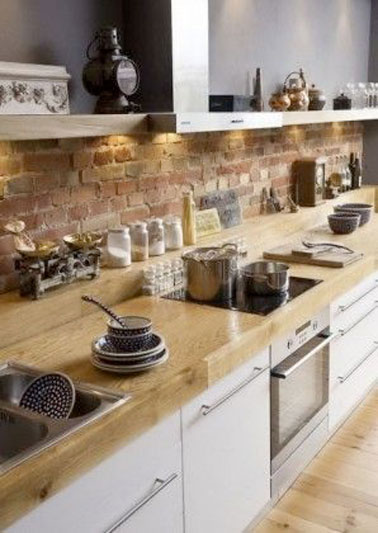 Crédence de cuisine en mur de brique mixée avec un plan de travail en bois et des meubles de cuisine blanc. Déco traditionnelle autour de la hotte avec une balance chinée et des petits chaudrons en cuivre 