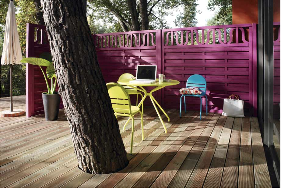 Pour aménager une terrasse dans le jardin, une palissage bois peinte couleur prune et mobilier de jardin couleur vert et bleu