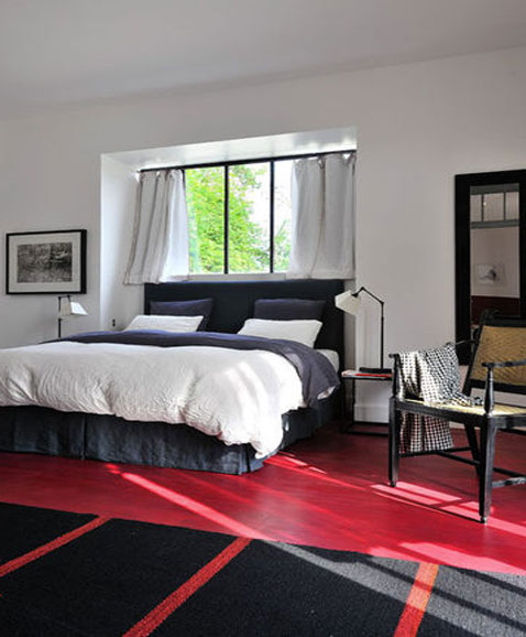 Décoration de chambre par Sarah Lavoine murs peinture blanche, sol peinture rouge brillant, tapis noir à petites rayures rouge, fauteuil design noir 