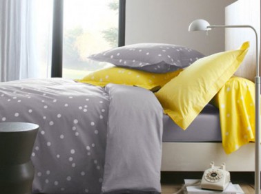 Déco d'une chambre d'adulte grise égayée d'une couleur jaune. La puissance du jaune des taies d'oreiller et du traversin illumine cette chambre construite autour du gris de la peinture murale et du linge de lit.