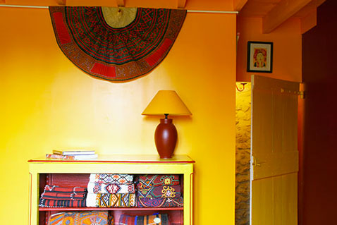 Une lumineuse peinture chambre couleur jaune associée à un rouge brique avec la lampe d'appoint et les tissus africains pour une déco de chambre où il fait bon vivre