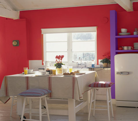pour une decoration de cuisine ambiance flashy peinture murale rouge cramoisi, etagère en bois peint en violet, coussin assorti sur tabouret de table