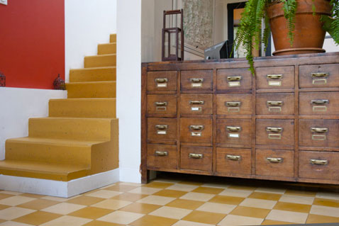 Déco d'une entrée maison avec un carrelage en damier couleur jaune et beige et l'escalier de ciment peint en jaune moutarde, un mélange de style heeureux avec le meuble de récup