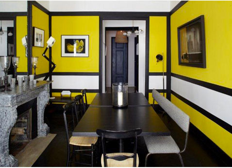 Ambiance déco moderne dans une salle a manger avec une peinture couleur jaune coupée d’une rayure blanche,sertie de noir. complétant le style, une grande table wengé noir, chaises et banc cuir blanc, applique murale et lampadaire design