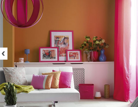 decoration salon couleurs vives peinture couleur orange associée à cadre photo et rideaux rose, plaid en laine vert anis suspension en bois fushia