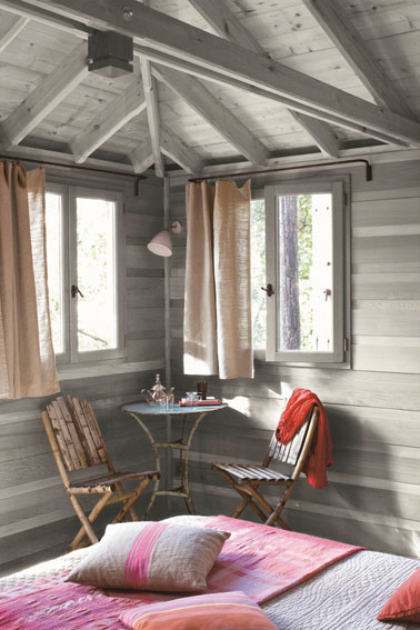Décoration d'une chambre gris et rose pour une ambiance douce et apaisante. Murs et plafond en planches lasurée grise s'harmonise avec le rose tendre des rideaux et le plaid et les coussins de lit gris et rose plus soutenu.