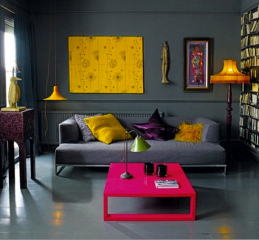 Dans un salon aux murs gris anthracite, pour apporter luminosité et dynamique, une table peinte en rose flashy, coussin et toile jaune intense