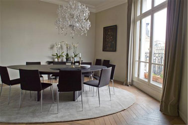Salle à manger aux lignes épurées et couleurs naturelles. Couleur peinture murale dans deux tons de gris taupe, rideaux gris plus soutenu, grand tapis rond gris perle, table et chaises noires. 