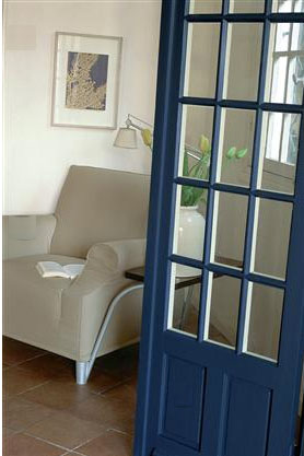Une déco de salon gris et blanc travaillée en contraste avec une peinture murale en gris blanc, un fauteuil dans un doux ton de gris mastic. Le bleu intense de la peinture de la porte crée un joli contraste 