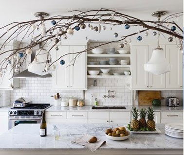 Une belle décoration de cuisine blanche pour Noël, faite avec une grande branche d'arbuste et des  boules de Noël dorées et argentées au dessus de la table de cuisine