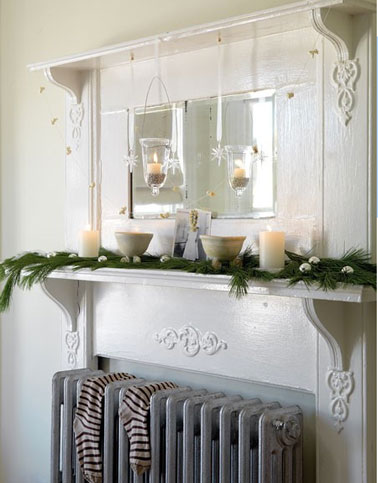 Décoration de Noël pour le coin radiateur du salon avec branchages de verdure, des bougies blanches et les traditionnelles boules de Noël argentées. Sur le radiateur les chaussettes attendent les cadeaux