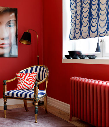 Un salon à la décoration ambiance boudoir contemporain. Peinture murale rouge vif, rideau bleu et blanc fauteuil style recouvert tissu rayé blanc et bleu