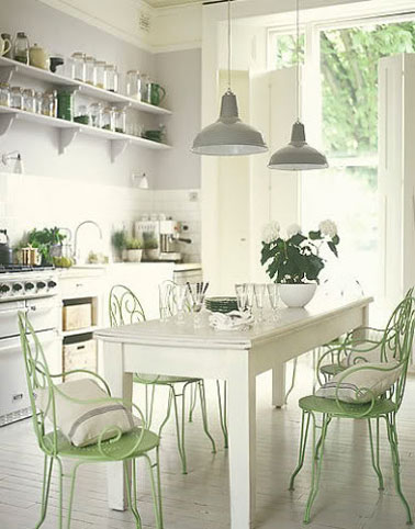 Une palette de couleurs tendres pour la déco d'une cuisine esprit maison de campagne.  Au dessus du carrelage blanc, le mur est repeint en gris perle, la table en bois a reçu un coup de peinture blanc cassé et les chaises de jardin repeintes en vert d'eau.
