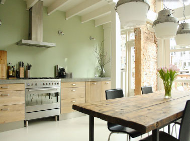 Superbe décoration d'une cuisine grande et lumineuse avec une peinture vert d'eau sublimé par la teinte ivoire des poutres apparentes repeintes. Design, les meubles de cuisine forment un contraste intéressant avec la table de ferme.  