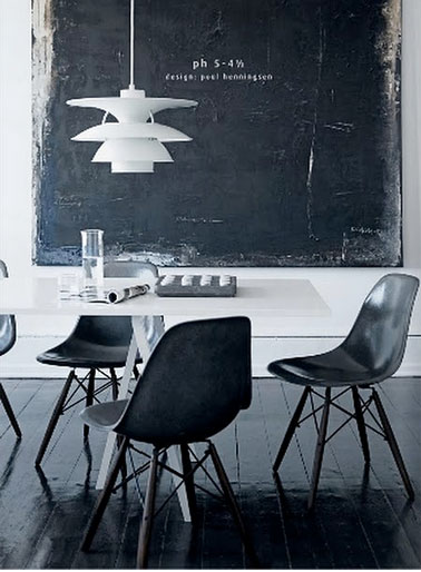 Salle à manger en noir et blanc avec un sol parquet peint en noir brillant. Au mur, grande peinture moderne monochrome noir sur mur blanc. Plateau de table laqué blanc, chaises noir.