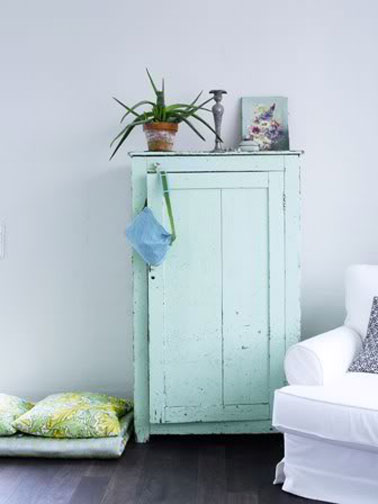 La fraicheur des couleurs pastel pour la déco d'un salon. Aux murs, une peinture blanche nuancée de bleu, le vert jade de la petite armoire est repris dans le tissu à fleur vert et jaune des coussins et le tapis de sol.
