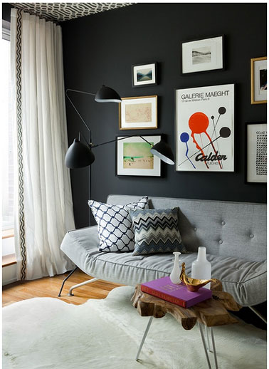 Pour la décoration de ce salon, harmonie de gris et noir. Aux murs peinture noir finition mat, canapé gris perle coussins tissu graphique gris et blanc. Tapis peau couleur ivoire 