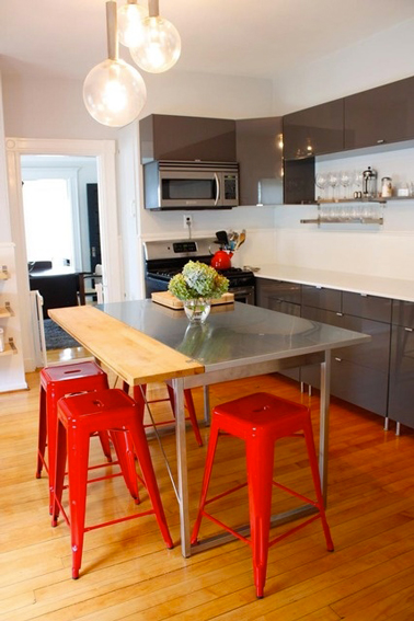 Une déco de cuisine rouge et grise où le rouge est apporté avec des tabourets Tolix qui mettent en valeur les meubles de cuisine gris et le plateau de table en inox