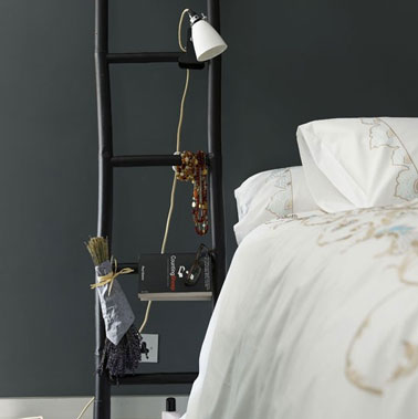 table de nuit dans chambre noir et blanc réalisée à partir d'une échelle en bois peinte en noir satin. Le spot de lumière est accroché sur une barre de l'échelle.