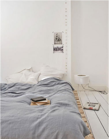 La déco d'une chambre ambiance zen avec un lit en palette dont le bois est laissé brut. Sur les murs peints en blanc pur une guirlande lumineuse borne l'espace de la tête de lit.