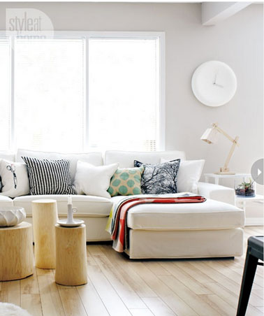 Un style résolument scandinave pour la décoration de ce salon. Au sol, un parquet de chene clair, peinture mural gris pastel, grand canapé d'angle en tissu blanc, chaise vintage et set de 3 tables basses en sapin blanc