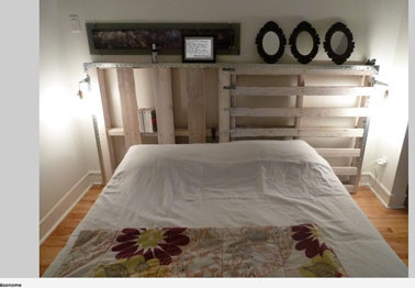 Lit chambre adulte fait avec des palettes bois. La tête de lit également en palette permet des rangements et sert d'étagère pour présenter des cadres photos