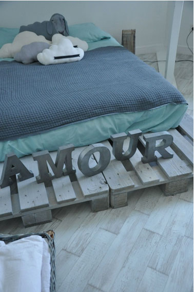 Une chambre d'ado bleu et vert clair qui affiche son slogan love sur un lit en palettes passées à la lasser gris bleu pour créer une harmonie avec la couleurs des murs et du sol de la chambre.