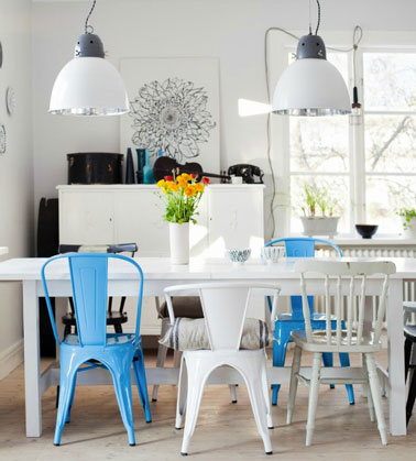 Salle à manger avec table blanche et chaises dépareillées bleu et blanc. Mélange de chaises Tolix peintes en bleu ou blanc et chaises bois de récup peintes en blanc