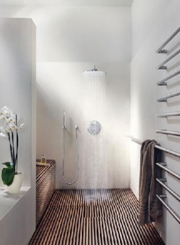 Reproduire dans sa salle de bain l'ambiance d'un spa c'est possible : Un receveur douche italienne XXL installé dans un espace ouvert sur le reste de la salle de bain aux murs blanc immaculé, un sol en teck façon caillebotis, un éclairage travaillé en indirect avec des spots encastrés, un pommeau de douche et une robinetterie Grohe conjuguant technologie et design, et prendre sa douche en version italienne commence. 