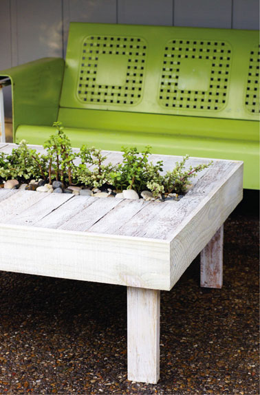 Table de jardin faite avec des palettes en bois. Au centre jardinière plantes aromatiques integrée dans plateau de table