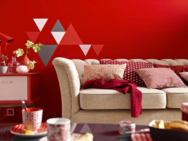 Une peinture rouge pour réveiller les murs du salon c'est top ! une idée déco à retenir :  Décorer le mur uni avec un pochoir de figures géométriques de différentes tailles et peints avec des couleurs en contrastes. Ici, le mur rouge s'éveille avec un jeu de motifs gris blanc et rouge plus clair