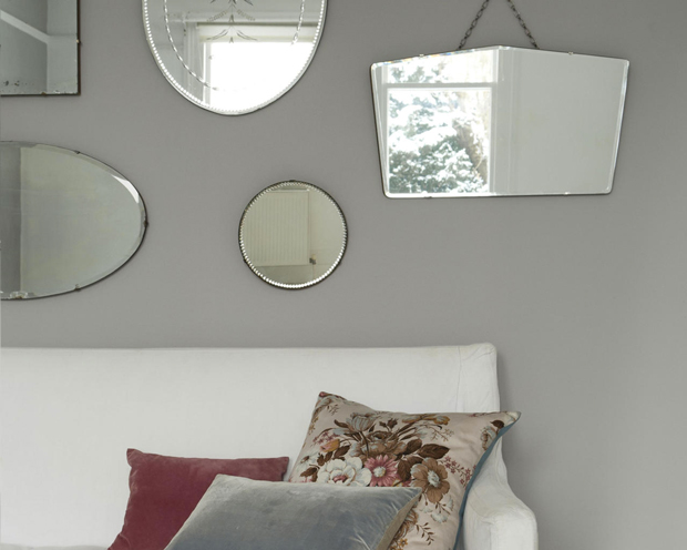 Couleur gris et blanc pour agrandir un salon : Petit salon couleur gris et blanc crème agrandi avec un jeu de miroirs de différentes tailles et formes accrochés sur le mur faisant face aux fenêtres