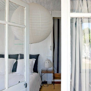 Une déco de chambre grise et blanc qui mise sur la simplicité et la combinaison des lignes : verticales pour le rideau de porte à rayures noires et grises, ronde avec la suspension en papier japonais et 2 carrés noirs apportés par les taies d'oreillers.