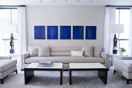 salon bleu et gris. Peinture murale et canapé cuir couleur gris perle, aux murs, serie de toiles couleur bleu Klein.  