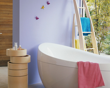 Déco salle de bain contemporaine. Autour de la baignoire design, peinture murale couleur lilas complétée de touches de couleurs vives avec les draps de bain rose bleu et jaune