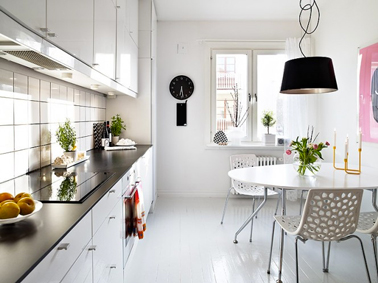La blancheur immaculée des murs et du mobilier de cette grande cuisine permet de diffuser largement la luminosité dans la pièce. Une lumière naturelle donc qui vient magnifier la décoration subtile composée de plantes vertes et d’autres accessoires noirs faisant un écho direct au plan de travail en granit noir également. 