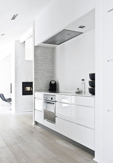 Ouverte sur le salon, cette cuisine se pare de ses atouts déco design pour sublimer la couleur blanche qui la compose largement. Les meubles laqués blancs reflètent la lumière de cet espace ouvert en relevant la modernité de certains éléments tels que le petit retour de mur impression pierre apparente gris ou encore le sol gris clair. Quelques touches de noir apportés par des objets décoratifs permettent d’appuyer la déco tendance et contemporaine de cette cuisine esthétiquement sans défaut.
