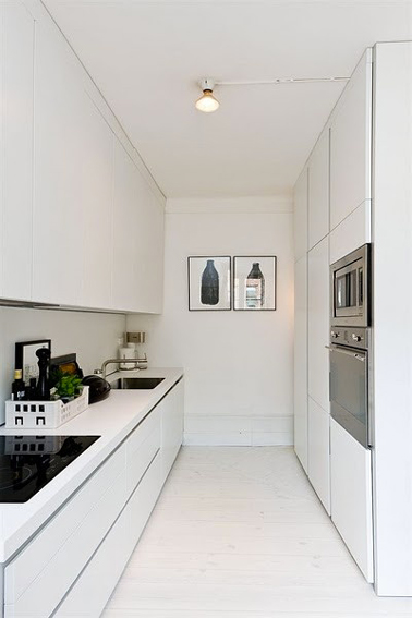 Une cuisine longue parfaite toute en blanc Les pièces qui s’étalent en longueur sont plus compliqués que d’autres à décorer. Et pour cause ! Il faut tenir compte de l’espace réduit et essayer de l’agencer afin de le rendre plus spacieux. Dans cette cuisine le pari est réussi puisque la peinture blanche s’étale sur les murs et les meubles afin de créer une sensation de profondeur dans ce coin cuisine tout en longueur. Les volumes sont rééquilibrés grâce à la présence de quelques objets électroménagers noirs et inox mais aussi le tableau mural qui délimite bien l’espace. Une déco idéale donc pour les cuisines des petits appartements ou studios !