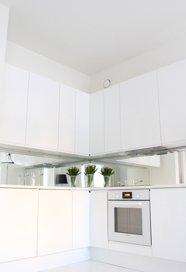 Une cuisine toute de blanc vêtue qui joue l'effet miroir sur la crédence Le total look blanc habille cette cuisine ! Des meubles de rangements muraux hauts et bas au design blanc simple et géométrique se chargent de rendre la pièce pratique et lumineuse. Et pour réveiller le caractère de cette pièce pure, une crédence au revêtement miroir donne une impression de profondeur tout en modernisant la déco autour des fourneaux.
