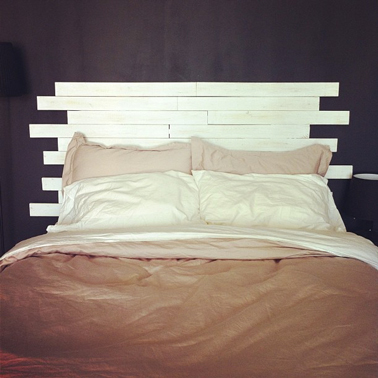 Une tête de lit en bois hyper sympa à faire avec des lames de parquet de récup. Le coté sympa est apporté avec les lames de bois longueurs inégales et le contraste couleur entre le mur noir et la tête de lit peinte couleur ivoire