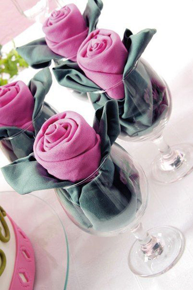 Un pliage en forme de bouton de rose réalisé avec deux serviettes présentées dans un verre à vin
