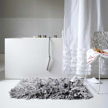 Ambiance apaisante dans cette salle de bain en dégradé de gris et blanc pour la peinture murale le rideau de douche en coton blanc et le tapis à longs poils gris soutenu