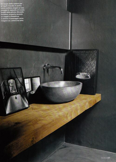 Du béton gris anthracite pour les murs d'une salle de bain. vasque ronde en céramique gris étain sur plan vasque fabriqué avec des poutres en chêne scellées dans le mur.