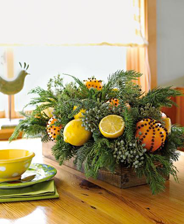 Un joli centre de table de Noël à faire facilement avec des branches sapin, des oranges piquées de clous de girofle, des citrons entiers et coupés pour un festival de couleurs fraiches sur la table 