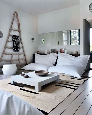 Une déco de salon où tout concourt à la convivialité. 4 poufs MyFab blanc en vis à vis remplacent les canapés, une peinture blanc grisé baigne la pièce dans une douceur absolue et une grande échelle en bois flotté posée en décoration murale rappelle l’histoire de cette ancienne ferme transformée en maison de vacances.