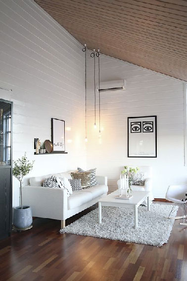 Une déco de salon blanc qui fait appel au bois pour dégager une ambiance chaleureuse. Compensant l'aspect neutre du blanc, le plafond en lambris et le parquet enveloppent le salon d’une atmosphère sereine et conviviale