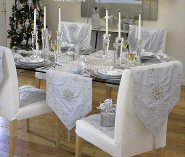 Déco table de Noël à la fois simple et magique avec des chemins de tables blanc et argent et des bougeoirs en verre. Les chaises sont recouvertes pour l'occasion du même chemin de table